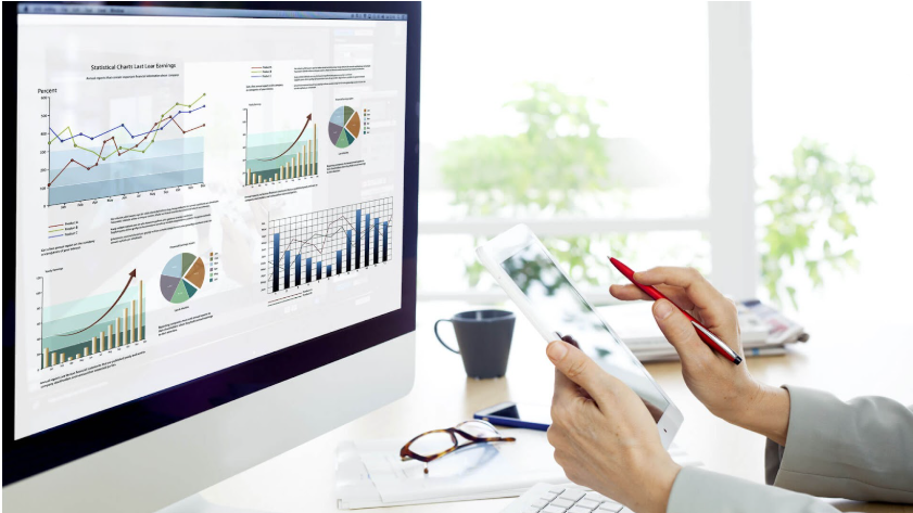 Choosing the Right Web Design Agency and Development in Melbourne 5 A person at a Melbourne web design agency holds a tablet and pen, studying a computer screen filled with various charts and graphs. A coffee cup rests on the desk, while the background reveals a bright room adorned with plants. | Ven Agency